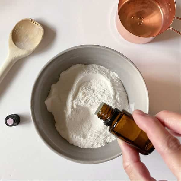 a bowl of baking soda a bottle of lemon essential oil and a spoon