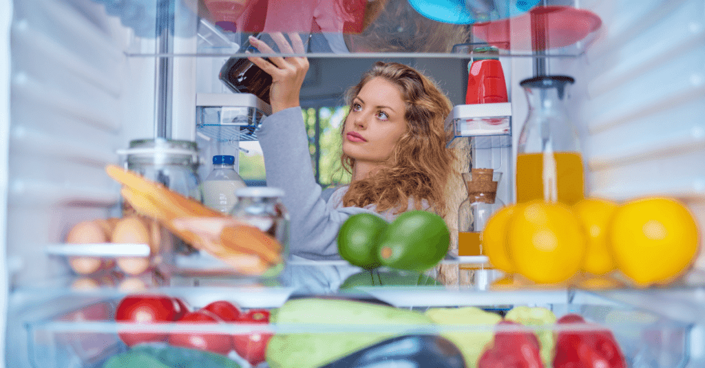 a lady standing in front of fridge having fresh vegetables and fruits