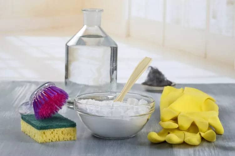 a jar of vinegar with a bowl of baking soda, gloves sponge and brush