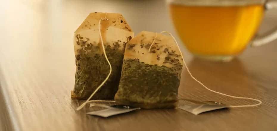 two used tea bags placed in front of a green tea cup 