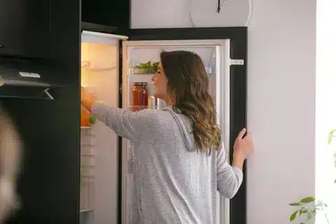 A side view of a woman with her fridge opened