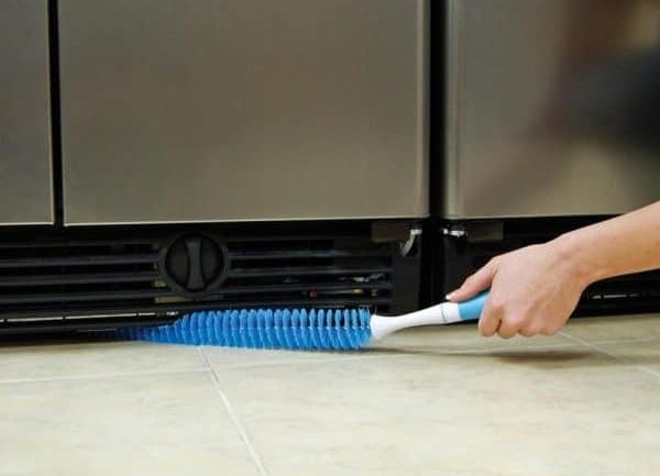 A view of a person cleaning the fridge coils with a brush