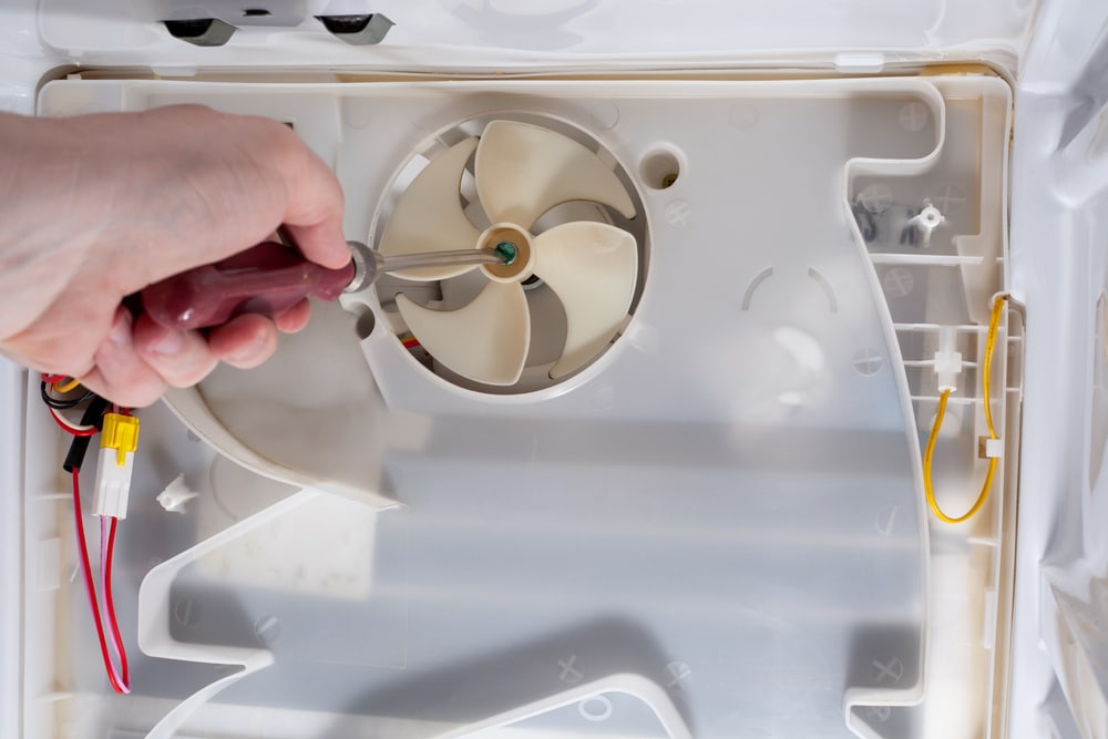 A view of a person holding screw diver in front of a fridge fan