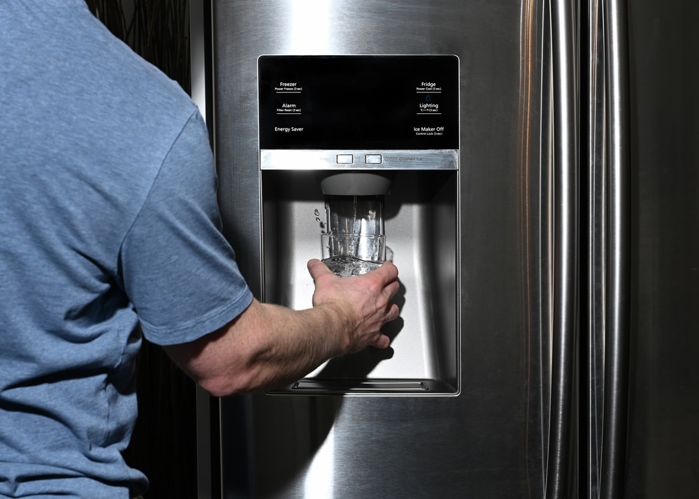 A view of a person taking out water from a fridge dispenser