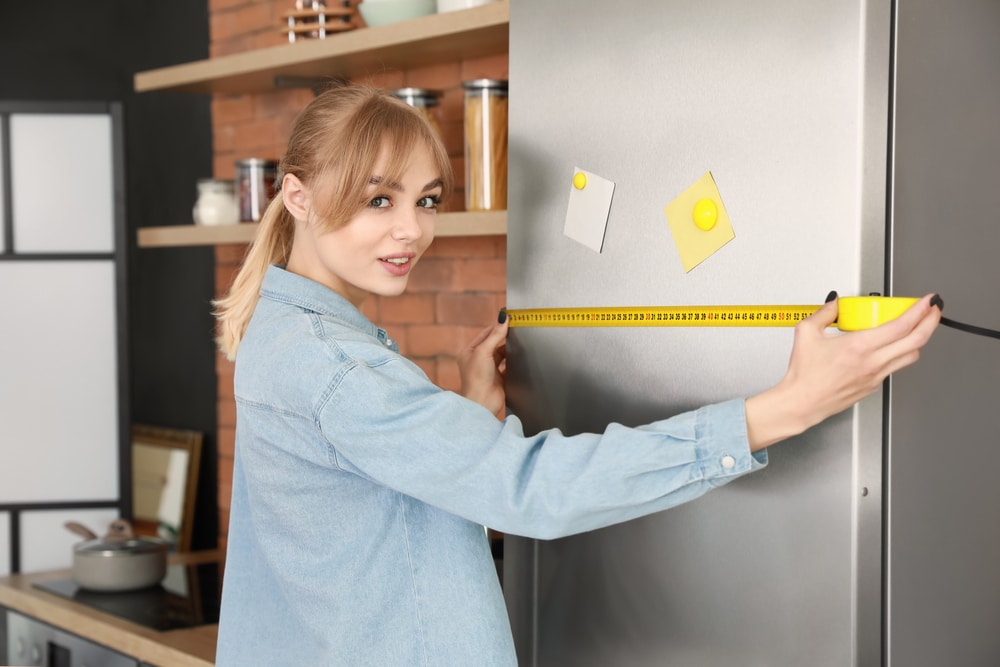 A view of a lady measuring a fridge with an inches tape