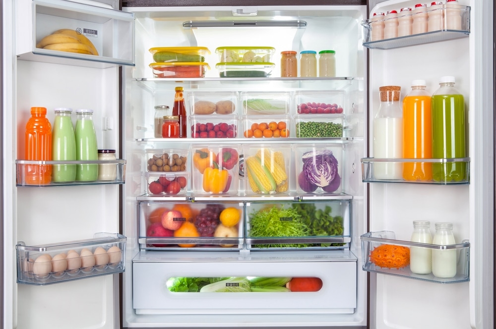 plastic containers with different fruits and vegetables in a open fridge. frozen food storage.